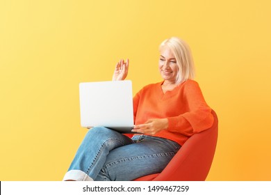 Mature Woman With Laptop Sitting On Chair Against Color Background