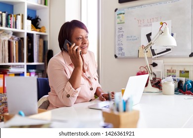 Mature Woman With Laptop Working In Home Office Using Mobile Phone