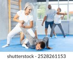 Mature woman learns how to do painful hold with trainer in the gym. Self-defense lesson