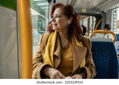 mature woman listens to music with headphones while traveling in public transport on the way to work - Powered by Shutterstock