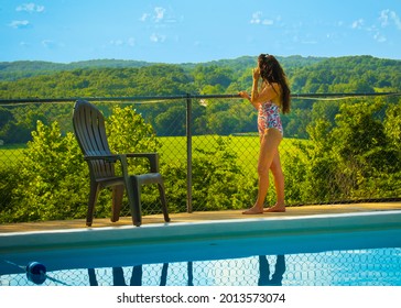 Mature Woman With Long Black Hair Dressed In Swimsuit  Standing In Outdoor Swimming Pool Area Enjoying View Of Valley Below