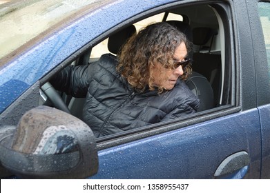 Mature Woman Looking Back Over Shoulder Driving Car Wet With Raindrops