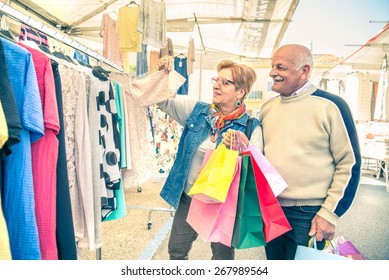 Mature Woman Looking Clothes At Market - Senior Couple With Shopping Bags Walking And Buying Some Dresses To Renew Wardrobe