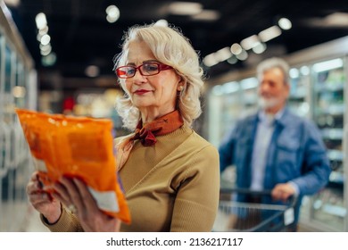 Mature woman looking at product at grocery store. Smiling woman shopping in supermarket and reading product information. Costumer buying food at the market. - Powered by Shutterstock