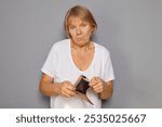 Mature woman looking sad holding empty wallet feeling poor and lost with financial problems reflecting depression and worry about bankruptcy standing isolated over gray background