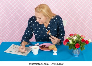 Mature Woman Making Crossword Puzzle In Newspapers In While Having Breakfast