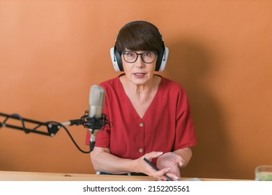 Mature Woman Making Podcast Recording For Her Online Show. Attractive Business Woman Using Headphones Front Of Microphone For A Radio Broadcast