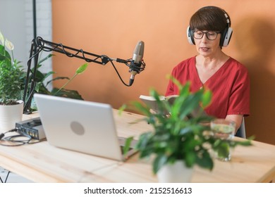 Mature Woman Making Podcast Recording For Her Online Show. Attractive Business Woman Using Headphones Front Of Microphone For A Radio Broadcast