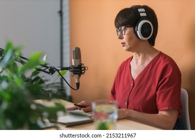 Mature Woman Making Podcast Recording For Her Online Show. Attractive Business Woman Using Headphones Front Of Microphone For A Radio Broadcast