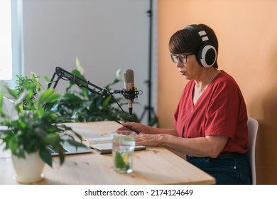 Mature Woman Making Podcast Recording For Her Online Show. Attractive Business Woman Using Headphones Front Of Microphone For A Radio Broadcast