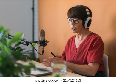 Mature Woman Making Podcast Recording For Her Online Show. Attractive Business Woman Using Headphones Front Of Microphone For A Radio Broadcast