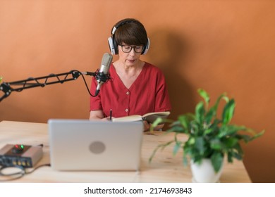 Mature Woman Making Podcast Recording For Her Online Show. Attractive Business Woman Using Headphones Front Of Microphone For A Radio Broadcast