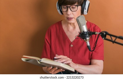 Mature Woman Making Podcast Recording For Her Online Show. Attractive Business Woman Using Headphones Front Of Microphone For A Radio Broadcast