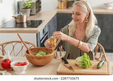 Mature woman making vegetable salad at table in kitchen - Powered by Shutterstock