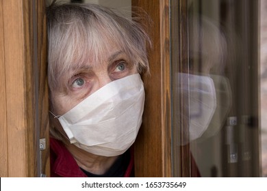 Mature Woman With Medical Mask Opens The House Door. Coronavirus Concept. Respiratory Protection. Quarantine At Home.