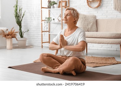 Mature woman meditating while sitting on floor at home - Powered by Shutterstock