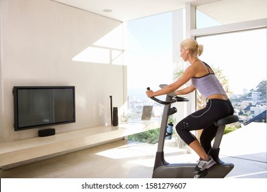 Mature Woman On Exercise Bike Watching Television At Home