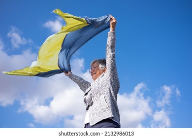 Mature Woman Outdoors Waves In The Wind A Scarf With The Colors Of The Ukrainian Flag In Support. Stop The War. Elderly Caucasian Woman With Short Hair Wearing Glasses.