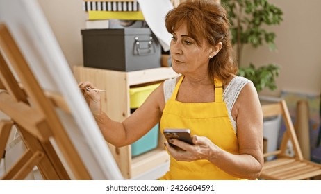 Mature woman painting on canvas in art studio while checking phone - Powered by Shutterstock