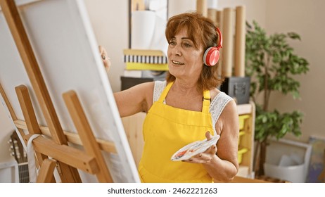 Mature woman painting in a studio with headphones, expressing creativity and enjoyment. - Powered by Shutterstock