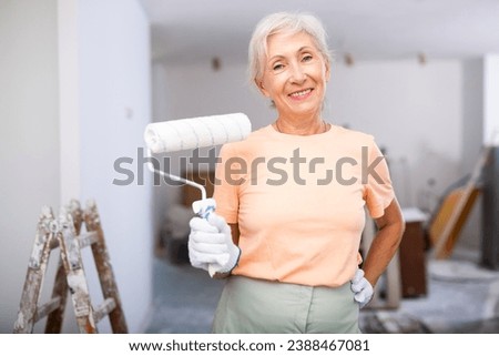 Mature woman painting walls with paint roller in a refurbished room