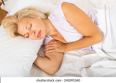 Mature Woman In Pajamas Sleeping With White Pillow In Bed At Home