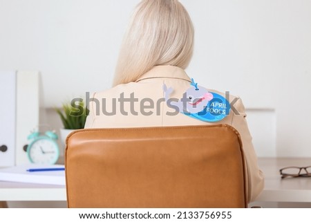 Mature woman with paper whale attached to her back in office. April fools day celebration