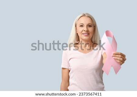 Mature woman with pink ribbon on grey background. Breast cancer awareness concept