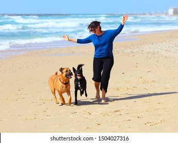 Mature Woman  Playing With Her Dogs On The Beach