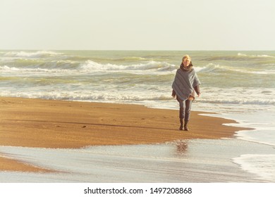 Mature woman with poncho that walks on the seashore in autumn - Powered by Shutterstock