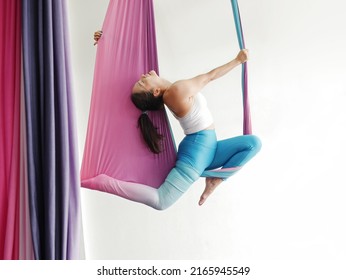 Mature woman pose in hammock performing aerial yoga or flying yoga exercise against white wall background in yoga studio room. Healthy lifestyles and emotional health of middle aged people concepts. - Powered by Shutterstock