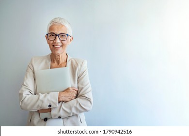 Mature woman posing against a gray background with laptop. Senior business woman standing against grey background with copy space. Portrait of successful woman feeling confident and looking at camera