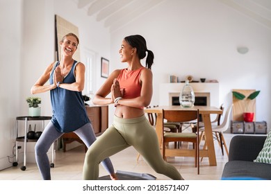 Mature woman practicing yoga at home with mixed race friend. Beautiful sporty indian woman with female friend in yoga position of the warrior at home. Two middle aged lady exercising at home, lockdown - Powered by Shutterstock