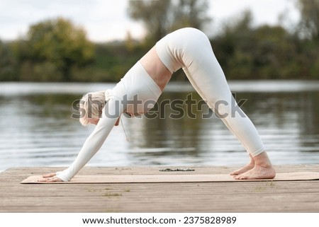 A mature woman practicing yoga, performing exercises on four limbs, push-ups from the floor, dog pose with its muzzle down, Adho Mukha Svanasana, training, dressed in sports clothes.