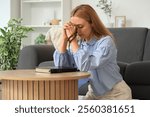 Mature woman praying with beads and Holy Bible on table at home