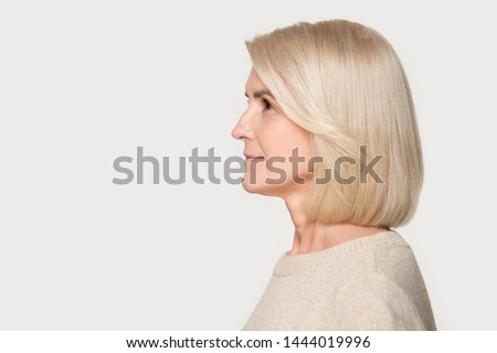 Mature woman profile view studio portrait isolated on gray background. Blond female with good styling, hairstyle side view headshot. Old lady looking to left, copyspace mockup template, blank space