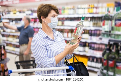 Mature Woman In Protective Mask Buying Bottle Of Wine In Store With Alcohol Drinks