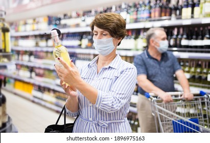 Mature Woman In Protective Mask Buying Bottle Of Wine In Store With Alcohol Drinks