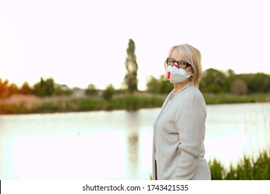 Mature Woman In Protective Respirator. A Woman Over 60 Years Old, Gray Hair In A Gray Blouse Looking At The Camera. Concept COVID-19. Elderly Lifestyle