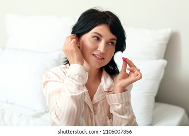 Mature Woman Putting Pink Ear Plugs In Bedroom