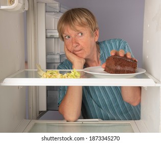 Mature Woman Reaching For Chocolate Cake Inside Fridge