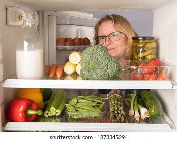 Mature Woman Reaching Into A Fridge Full Of Healthy Foods 