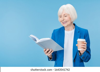 Mature Woman Reading Book With Cup Of Drink Over Blue Background