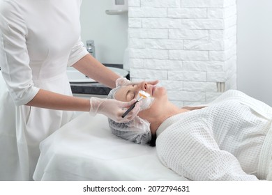 Mature Woman Receiving Wwhte Facial Mask In Spa Beauty Salon. Concept Of Skin Care For Older People