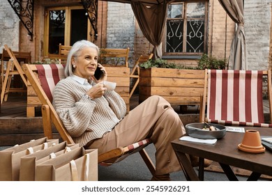 A mature woman relaxes outside, sipping coffee and chatting on her phone. - Powered by Shutterstock