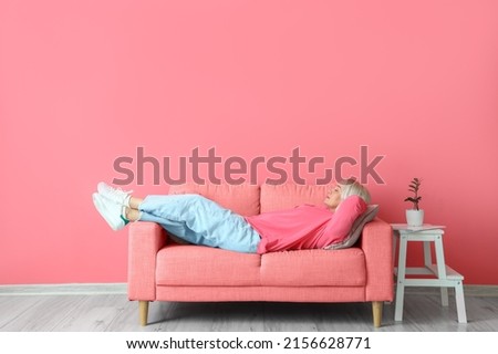 Mature woman relaxing on sofa near pink wall