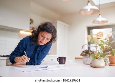 Mature Woman Reviewing And Signing Domestic Finances And Investment Paperwork In Kitchen At Home - Shutterstock ID 1841929651