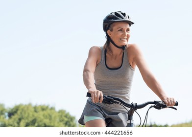 Mature Woman Riding On Mountain Bike In The Park. Portrait Of A Happy Senior Woman Riding Bicycle In A Park. Athletic Woman Wih Helmet Cycling And Looking Away.