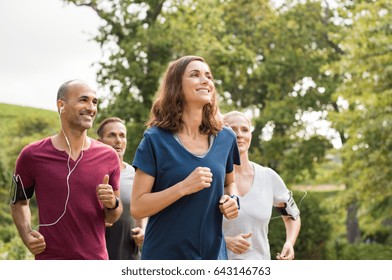 Mature Woman Running With Group Of People At Park. Happy Smiling Woman With Group Of Friends Running Together. Senior Runners Team On Morning Training.
