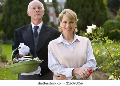 Mature Woman With Secateurs By Butler With Basket Of Gardening Tools, Smiling, Portrait